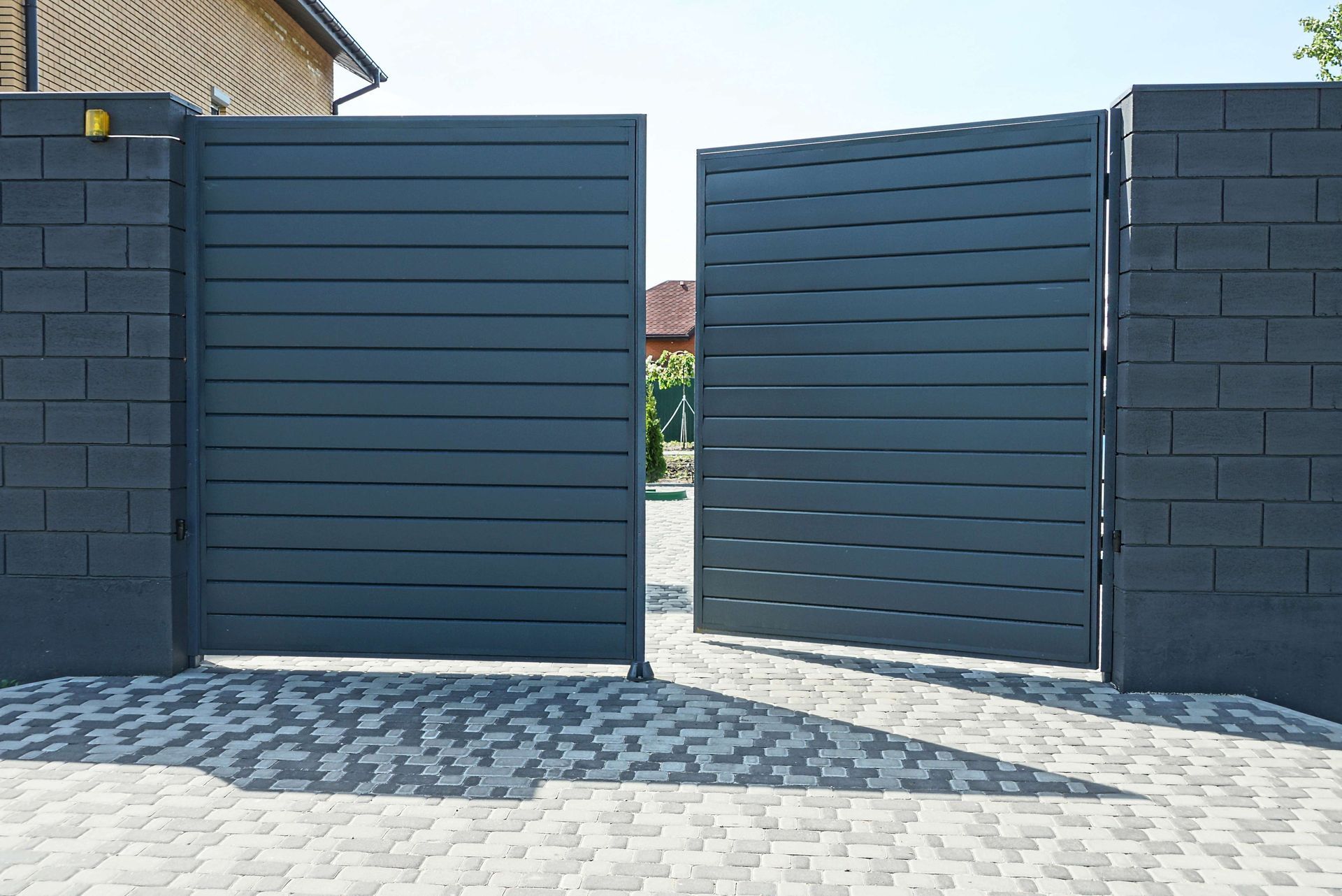 Open dark blue metal driveway gate in a paved courtyard between black brick walls Open dark blue metal driveway gate in a paved courtyard between black brick walls