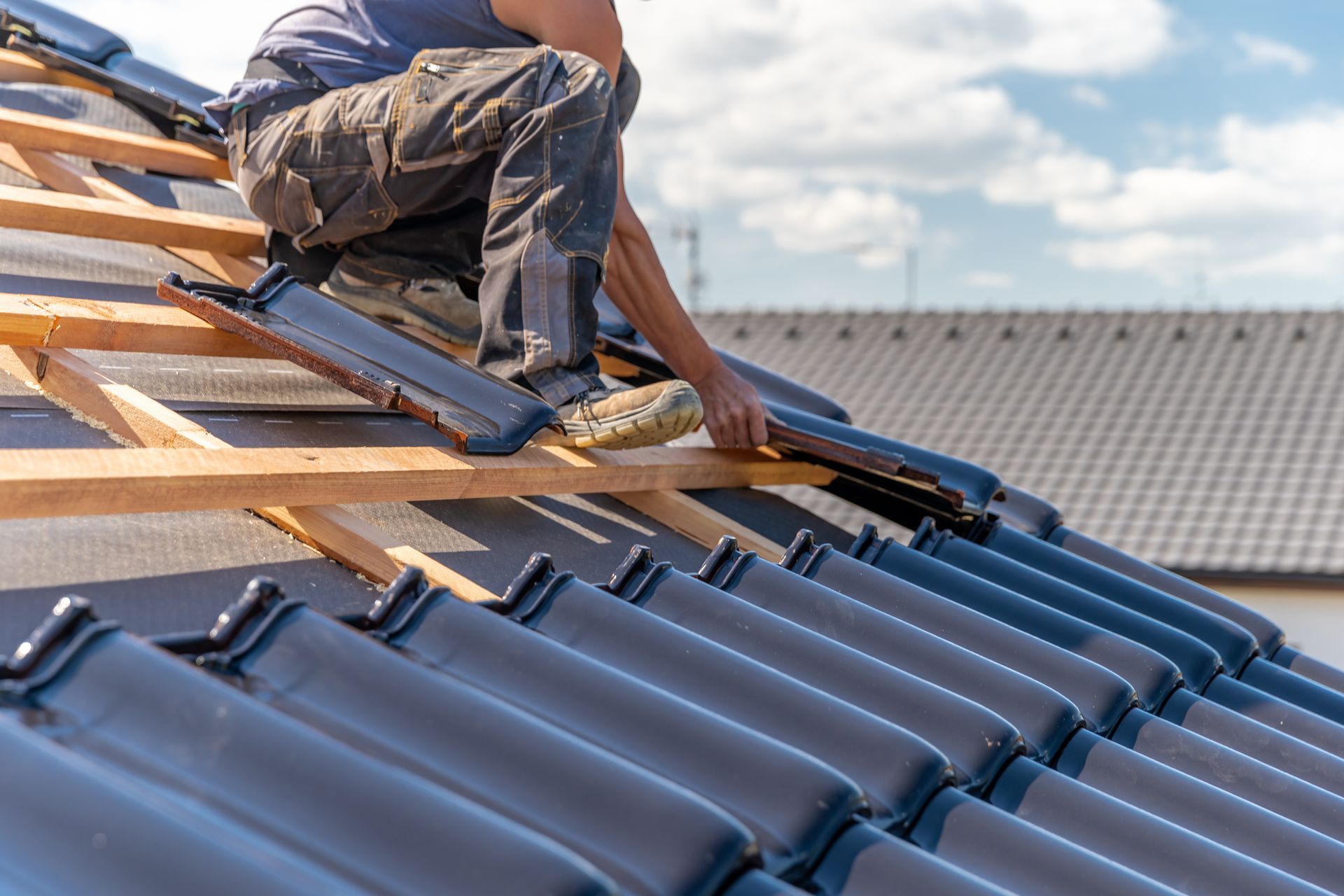 Worker installing blue roof tiles on a house roof