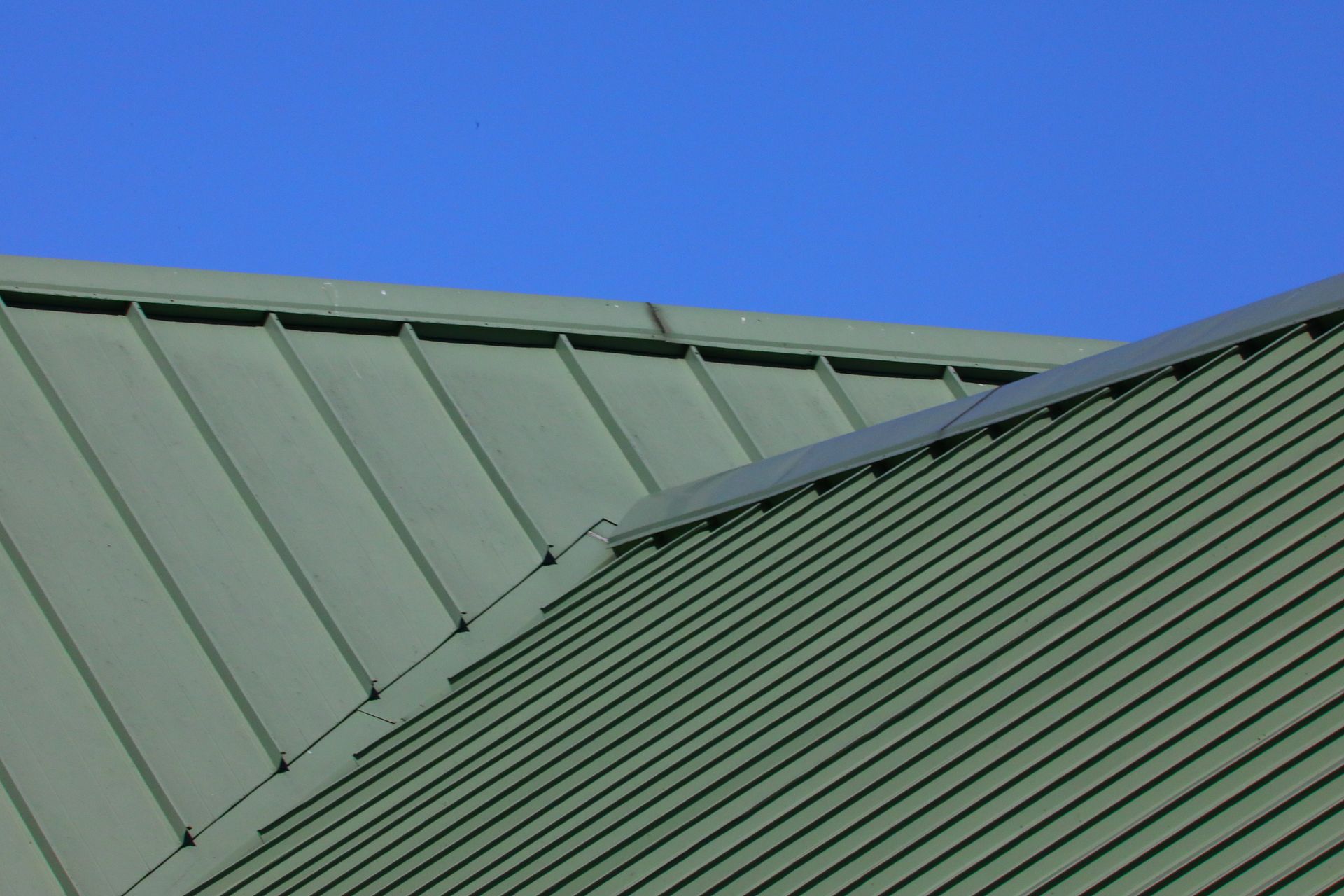 Green metal roof panels against a clear blue sky.