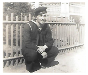 Sailor crouching by a wooden fence in a black-and-white photo