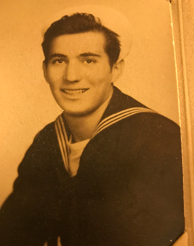 Sepia-toned portrait of a smiling person in a dark sailor-style uniform against a plain background