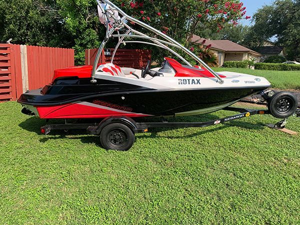 Red and black wakeboard boat on a trailer parked on grass in a yard