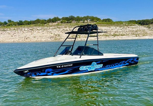 Blue-and-black speedboat on calm water near a rocky shoreline under a clear sky