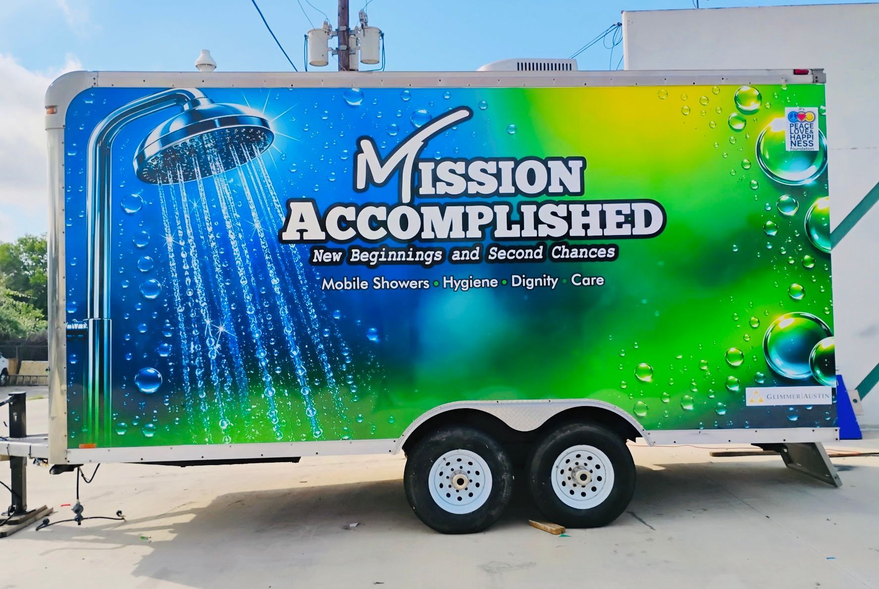 Green and blue trailer with “Mission Accomplished” logo, parked outdoors on a sunny day.