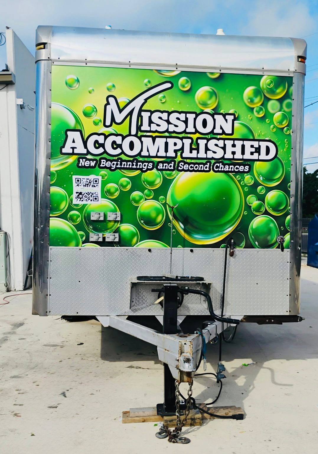 Food trailer with a green “Mission Accomplished” bubble design parked on a sandy beach.