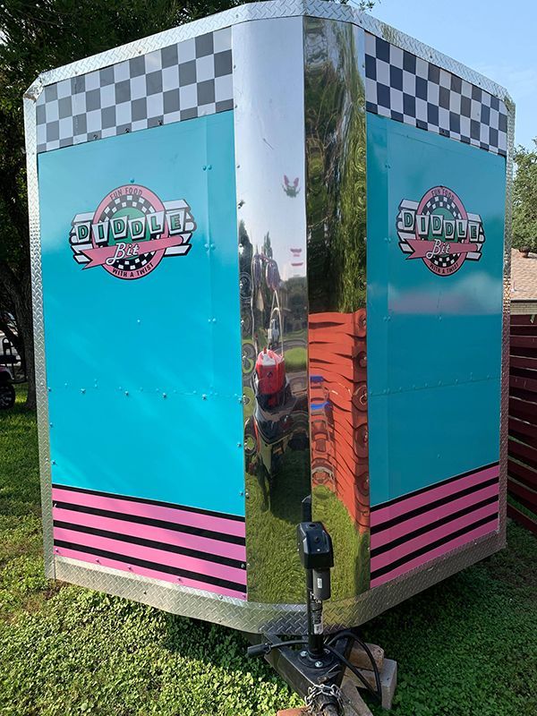 Turquoise concession trailer with checkerboard trim and pink stripes, shown on grass.