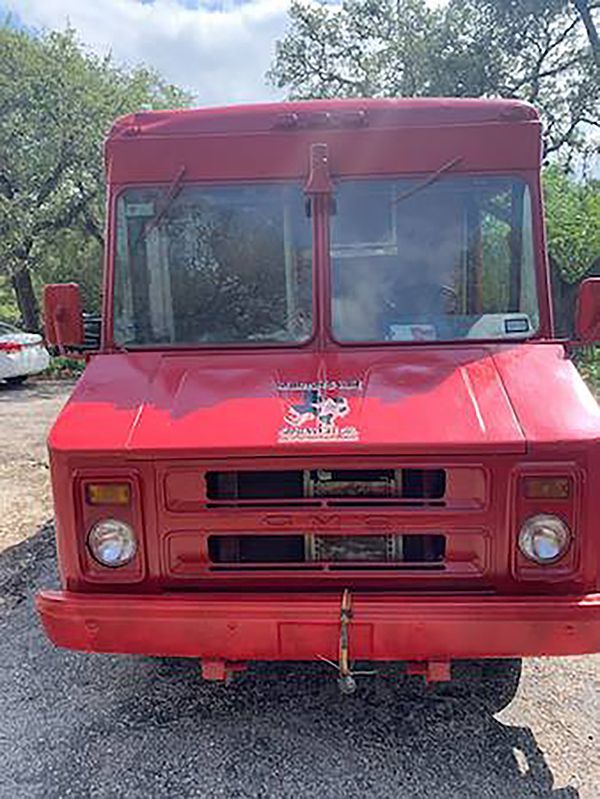 Front view of a red vintage truck parked on gravel outdoors