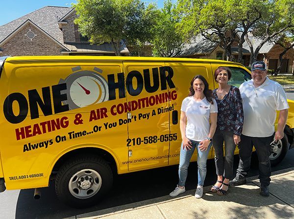 Three people standing beside a yellow One Hour Heating & Air Conditioning service van.