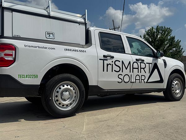 White TriSMART Solar service truck parked on a sunny street beside a metal building