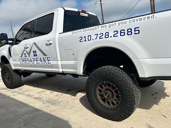 White Chesapeake roofing truck with company logo and phone number parked outdoors.