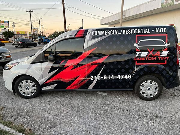 Wrapped black-and-red Texas Tint van parked on a street at sunset, with commercial/residential auto signage