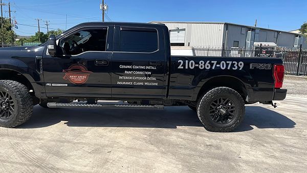 Black pickup truck with business decals and phone number parked outdoors in bright sun