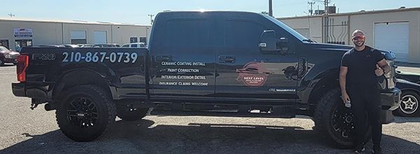 Black pickup truck with company lettering and phone number parked outdoors beside a man and motorcycle.