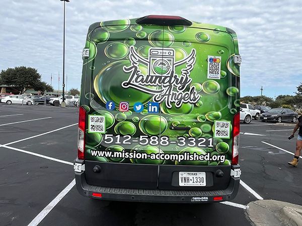 Green branded bus parked in a lot, with colorful graphics and the text “Mission Accomplished” and a phone number.