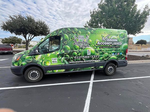 Green Mission Accomplished van parked in a lot, covered with clover graphics and contact text.