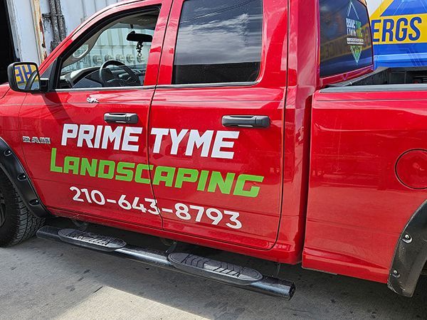 Red truck with “Prime Tyme Landscaping” logo and phone number on the door