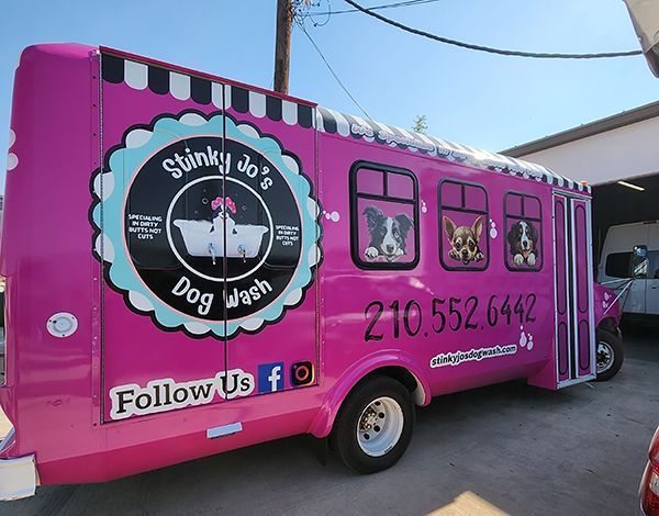 Bright pink dog wash trailer with business logo, phone number, and dog silhouettes parked outdoors.
