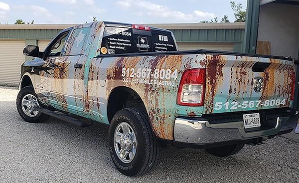 Wrapping vinyl on a black pickup truck with rust-colored design and phone number, parked outdoors