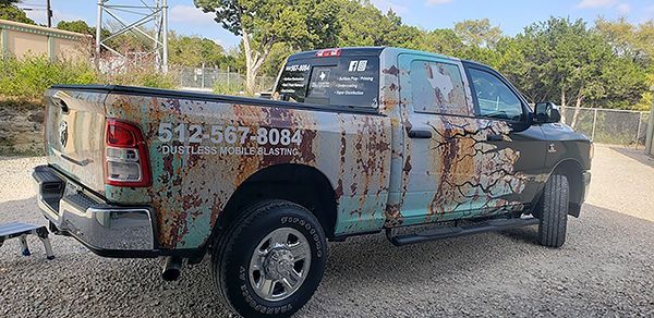 Rusty pickup truck with company decals parked on gravel beside a road in bright daylight