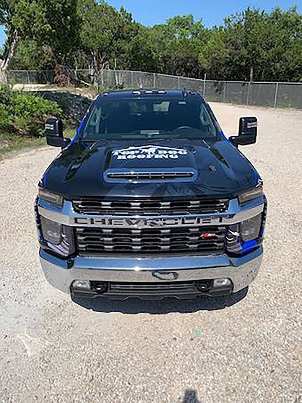 Blue and chrome Ford pickup truck parked on a gravel road with trees in the background.