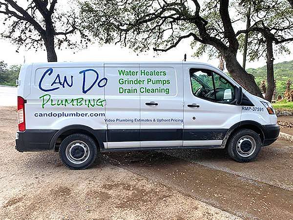 White Can Do Plumbing van with green lettering parked outdoors under trees.
