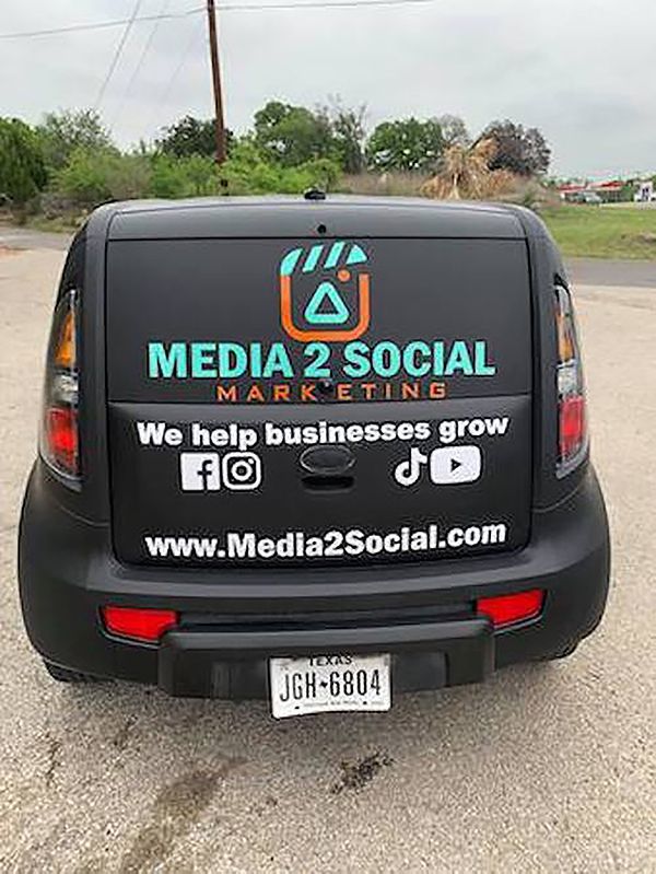Black van with “Media 2 Social Marketing” advertisement on the back, parked on a roadside.