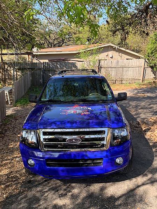 Blue Ford SUV parked in a driveway in front of a house, with trees casting shadows nearby.