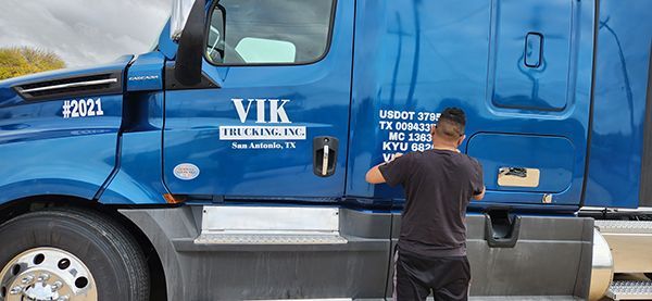 Blue VIK Trucking semi with a man working on the door in a lot