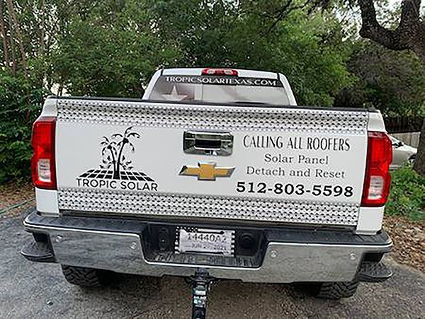 White pickup truck with “Calling All Roofers” and “Tropic Solar” decals, parked outdoors