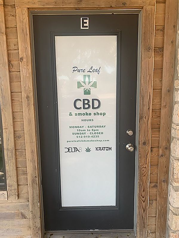 Black storefront door with white CBD smoke shop sign and floral logo above the handle