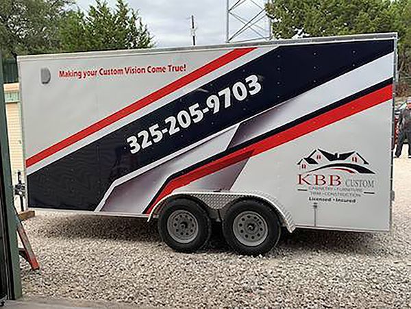 Black and white KBB Boston trailer with large phone number parked on gravel.