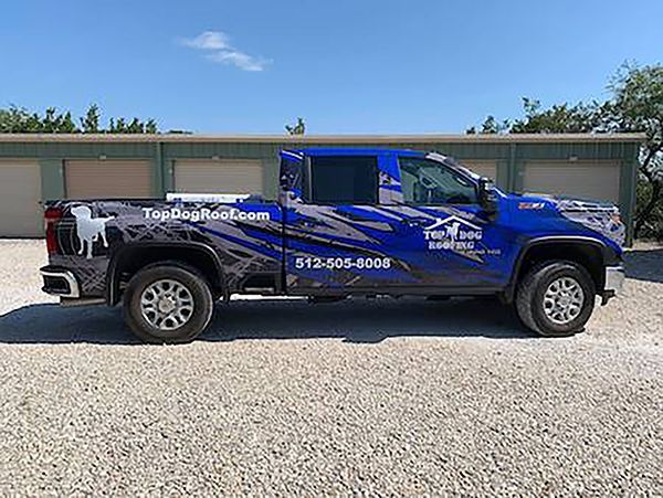 Blue work truck parked on gravel in front of storage units, with white company lettering on the side.