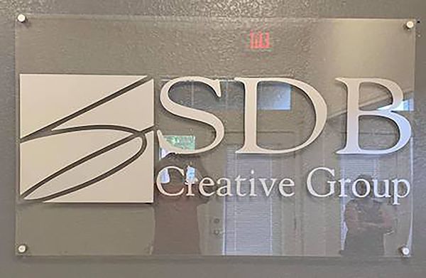 SDB Creative Group logo on a clear wall sign with metal standoffs