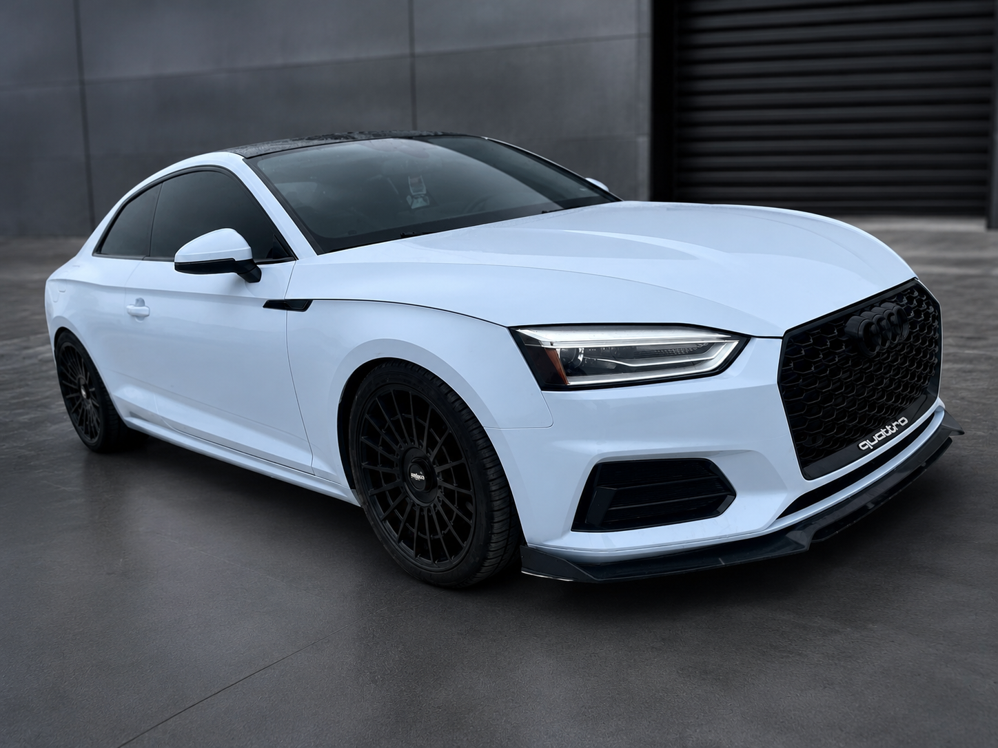 White sports sedan parked on wet pavement in front of a dark garage door