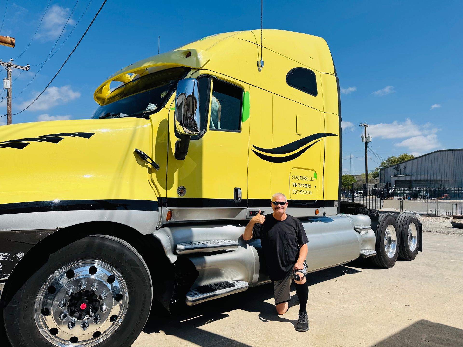 Man standing beside a bright yellow semi-truck on a sunny lot