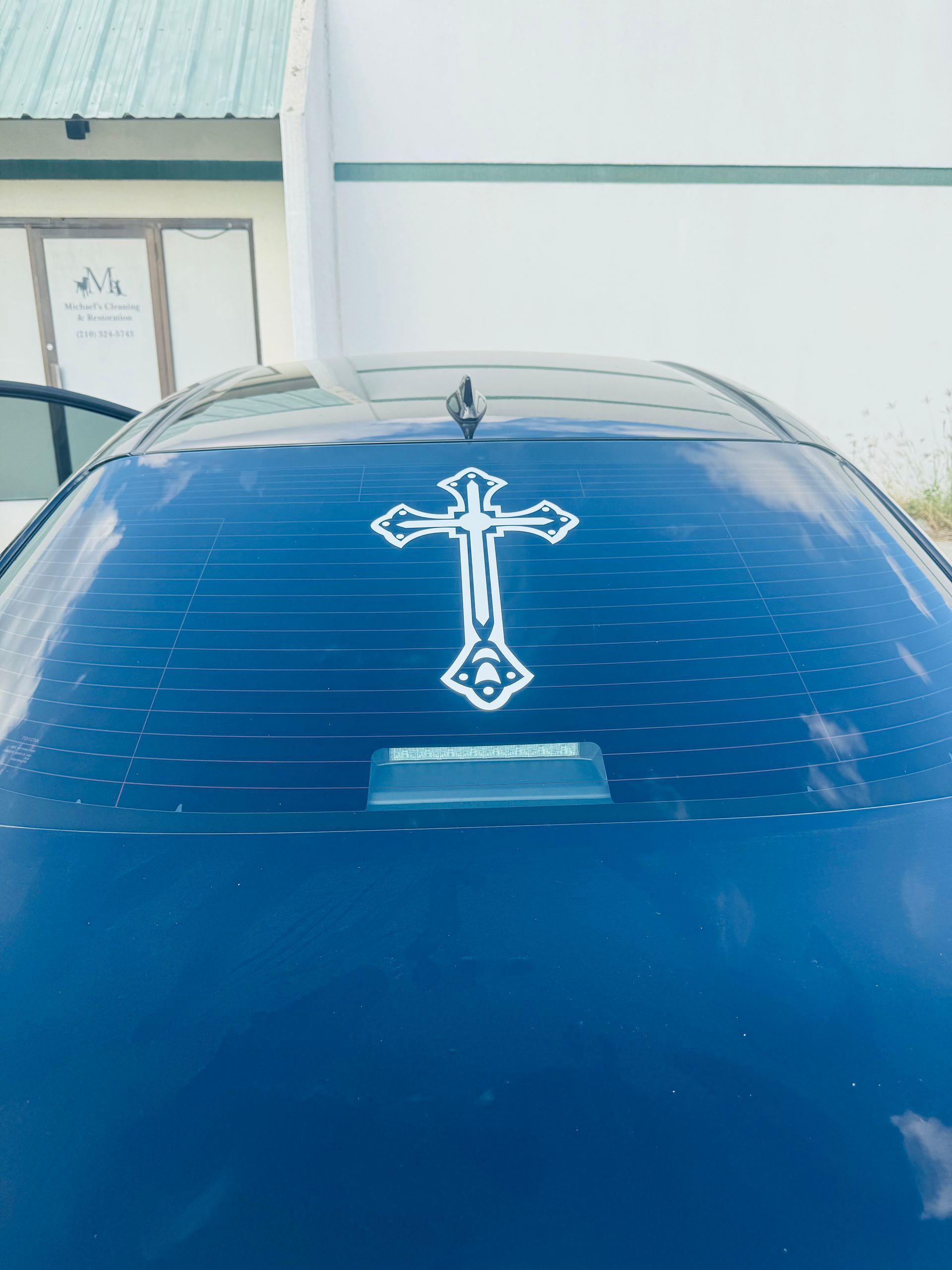 Blue car hood with a white cross emblem centered near the windshield, parked outdoors.