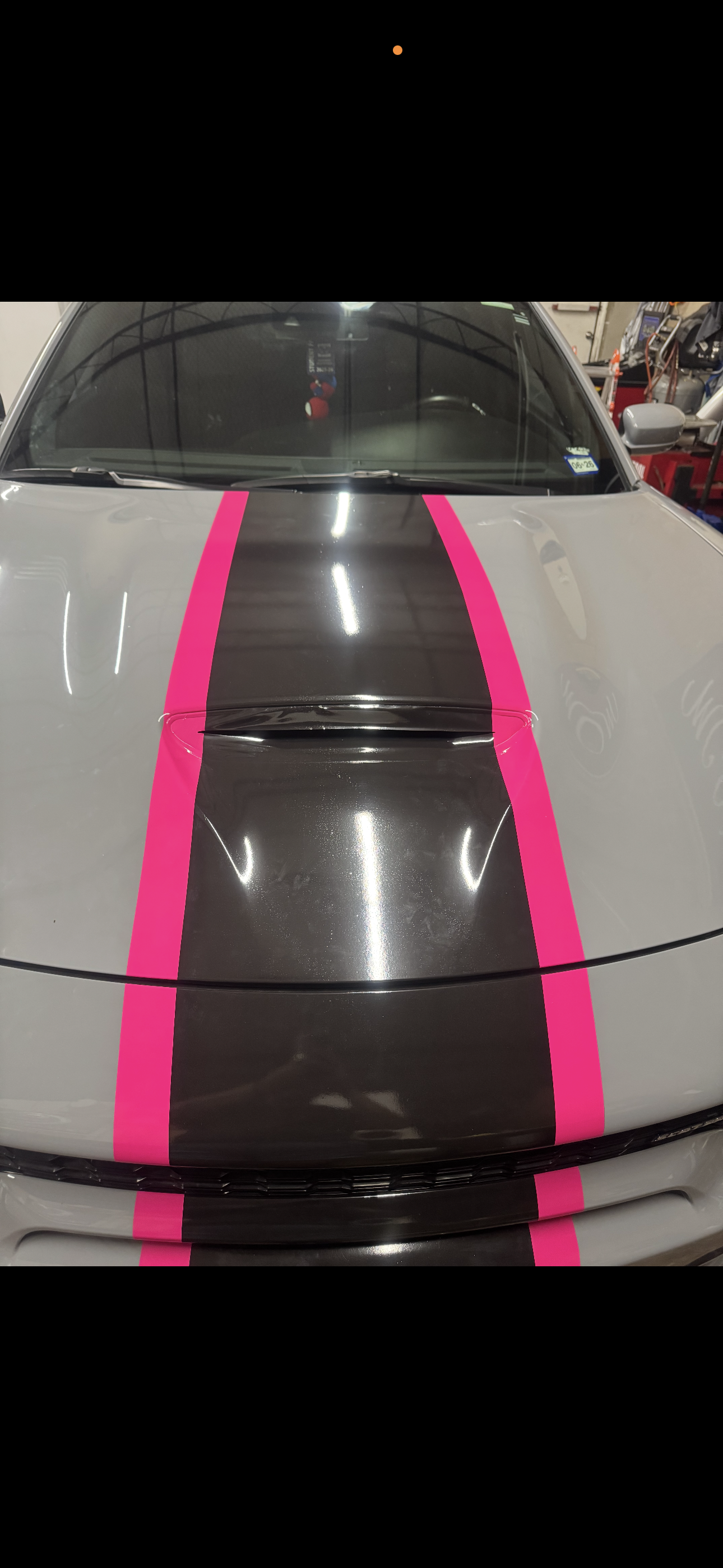 Front of a white car with a black hood and two bright pink racing stripes.