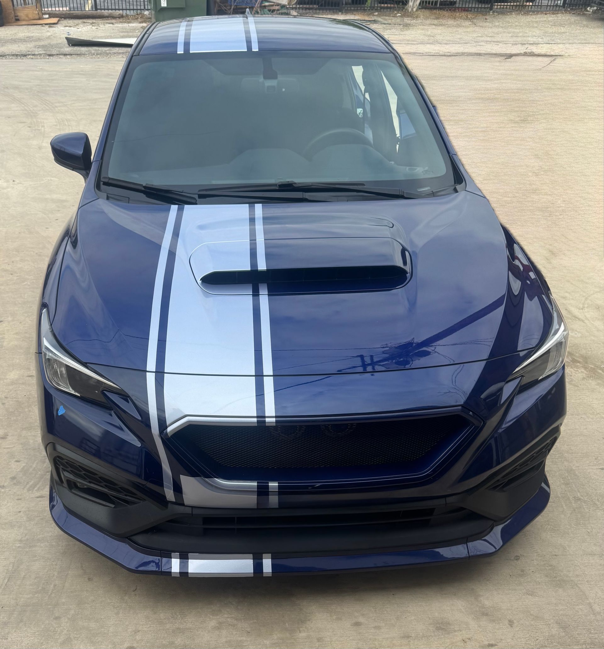 Blue sports sedan with white racing stripes, front view on a dirt lot