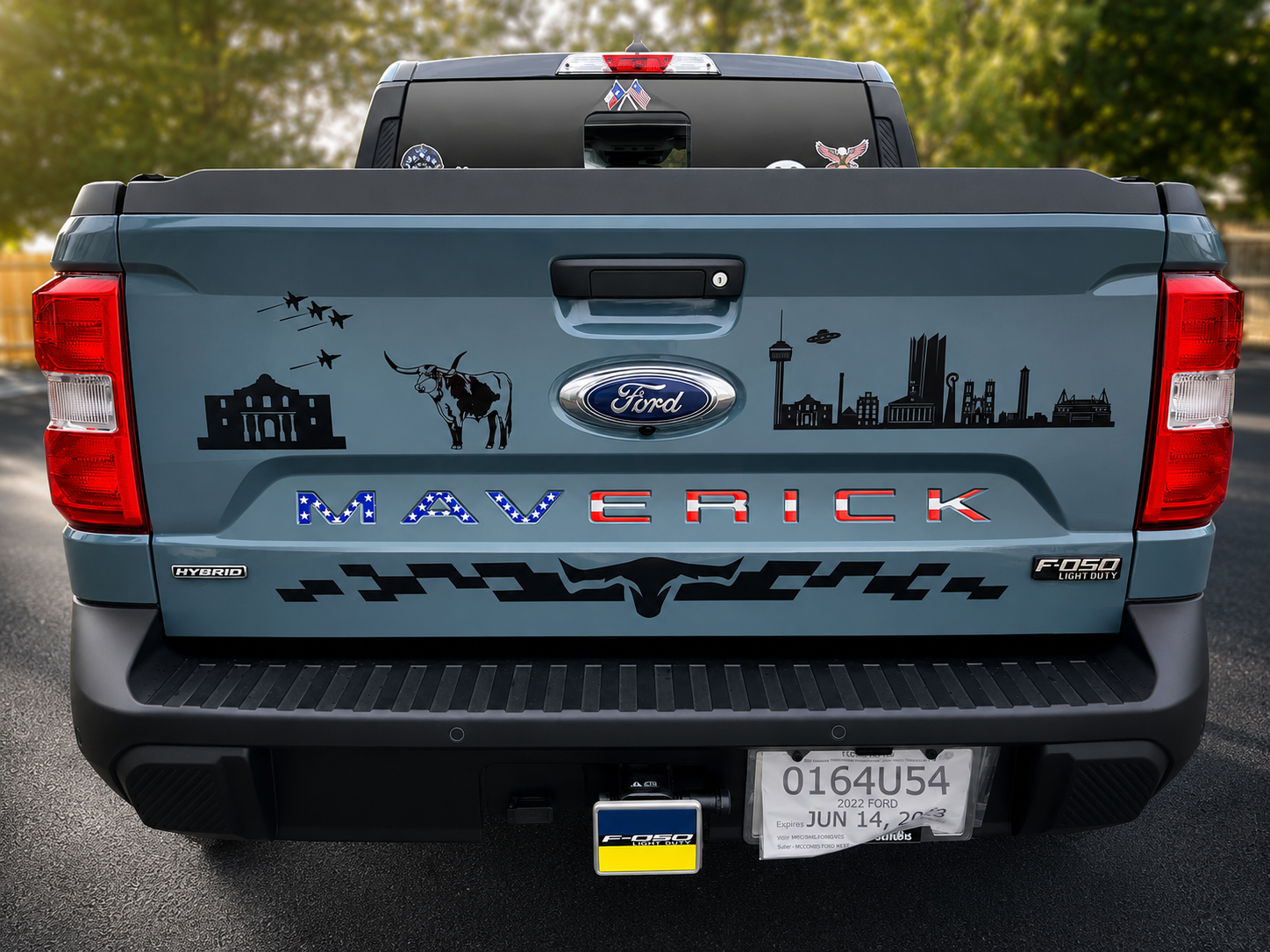 Blue Ford Maverick pickup truck rear with skyline and cow decals, parked outdoors.
