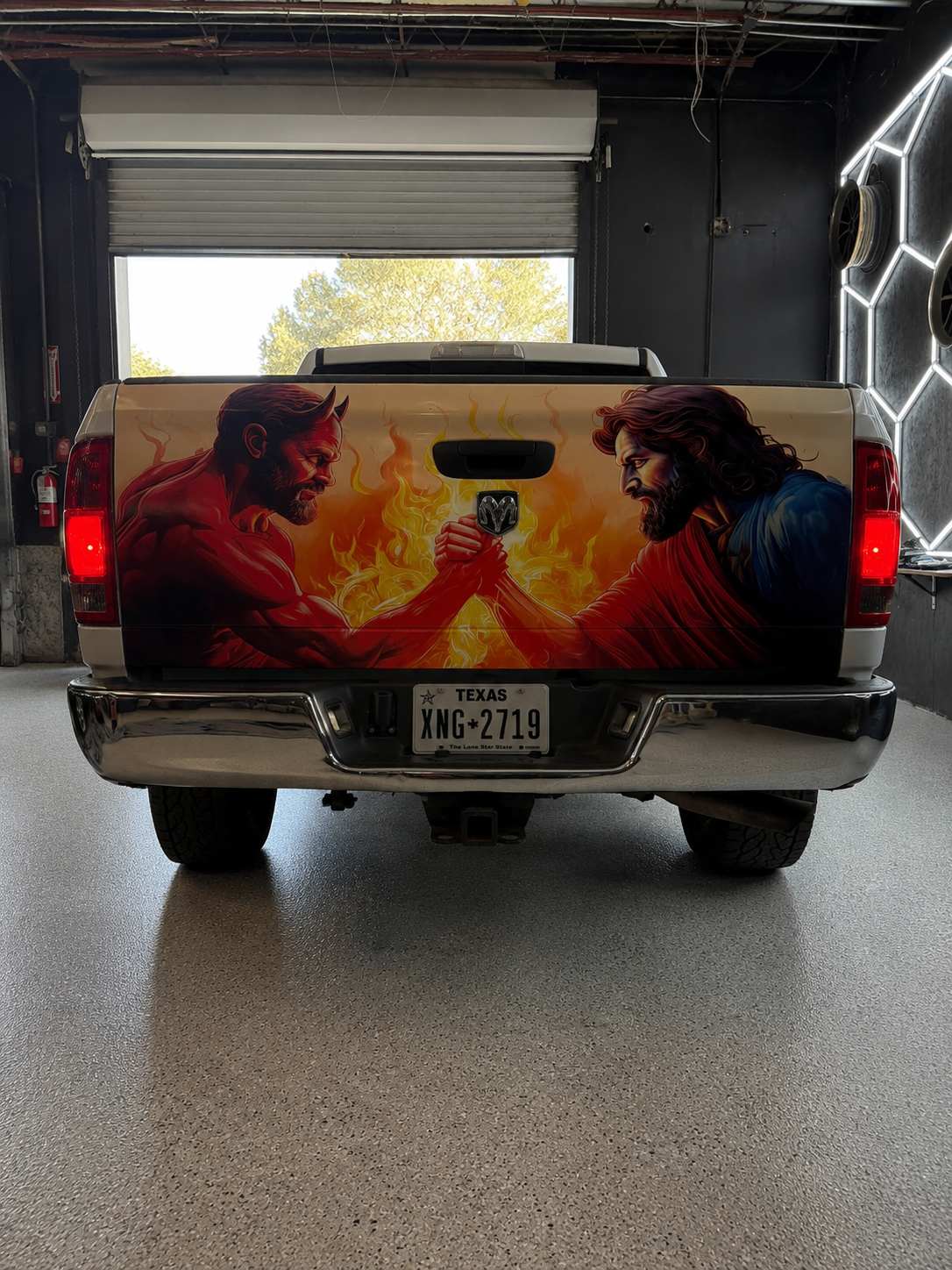 Pickup truck tailgate with a fiery face-off mural, parked inside a garage.