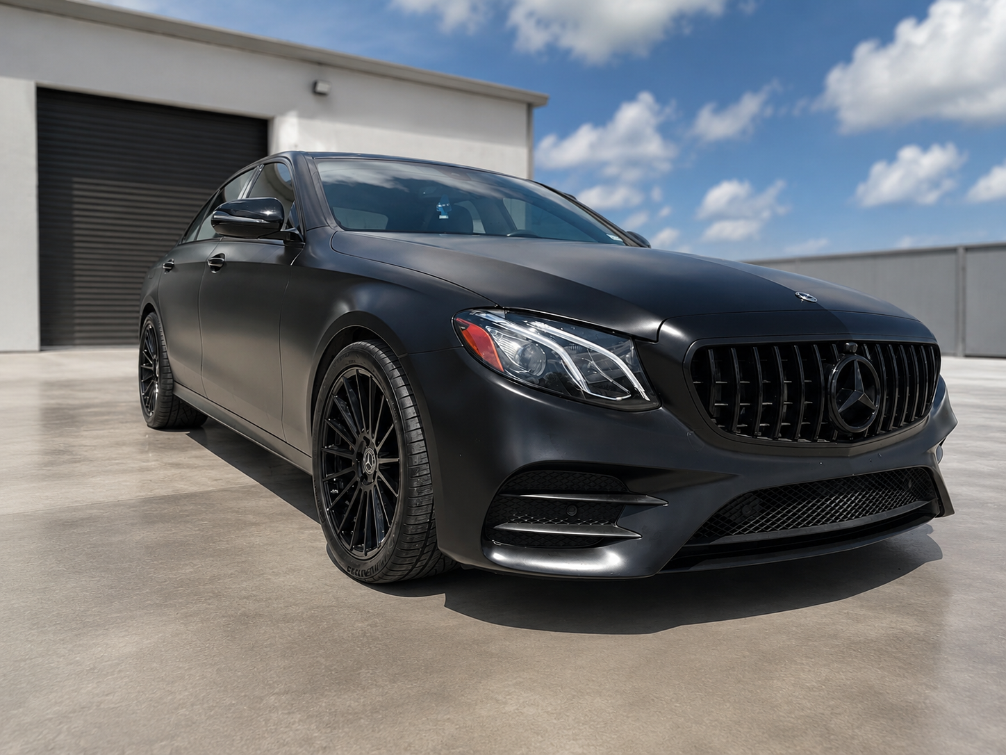 Black Mercedes sedan parked on a sunlit concrete lot outside an industrial building