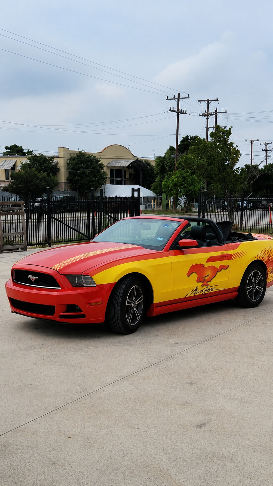 Red and yellow sports car parked on a street with a fenced background