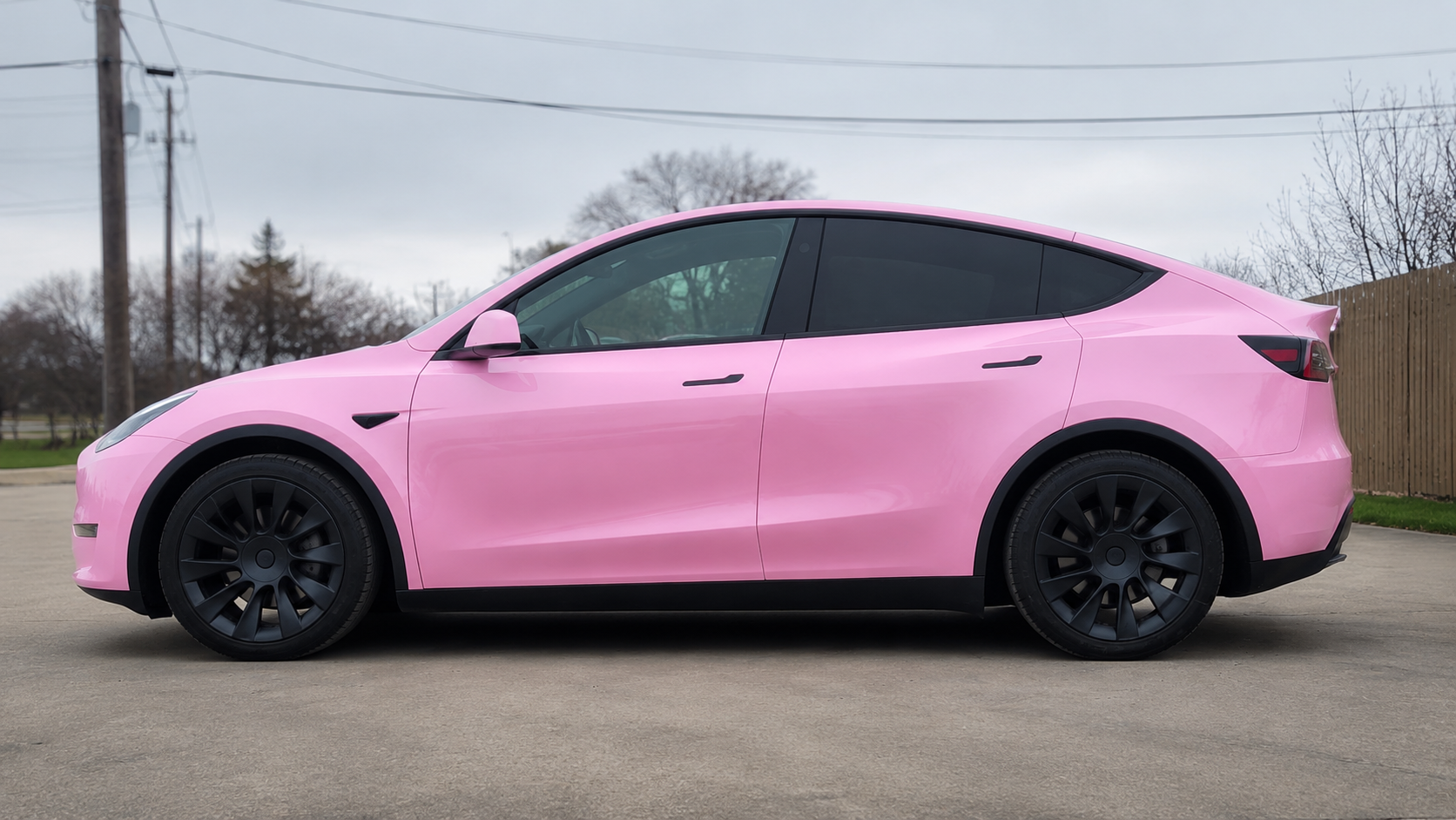 Pink Tesla SUV parked on a roadside under overcast sky