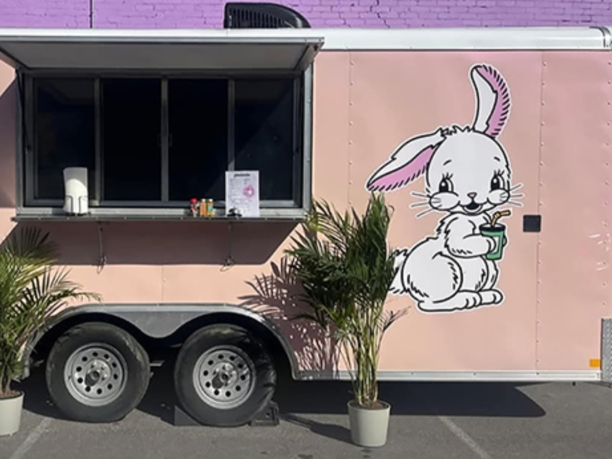 Pink food trailer with a bunny mural and service window, parked outside with potted plants nearby