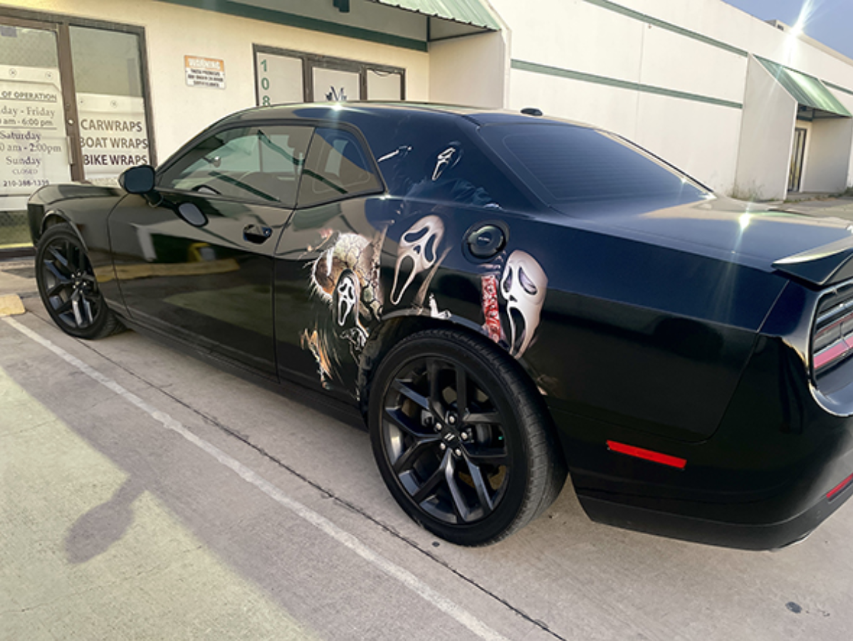 Black sports car with custom side graphics parked beside a building.