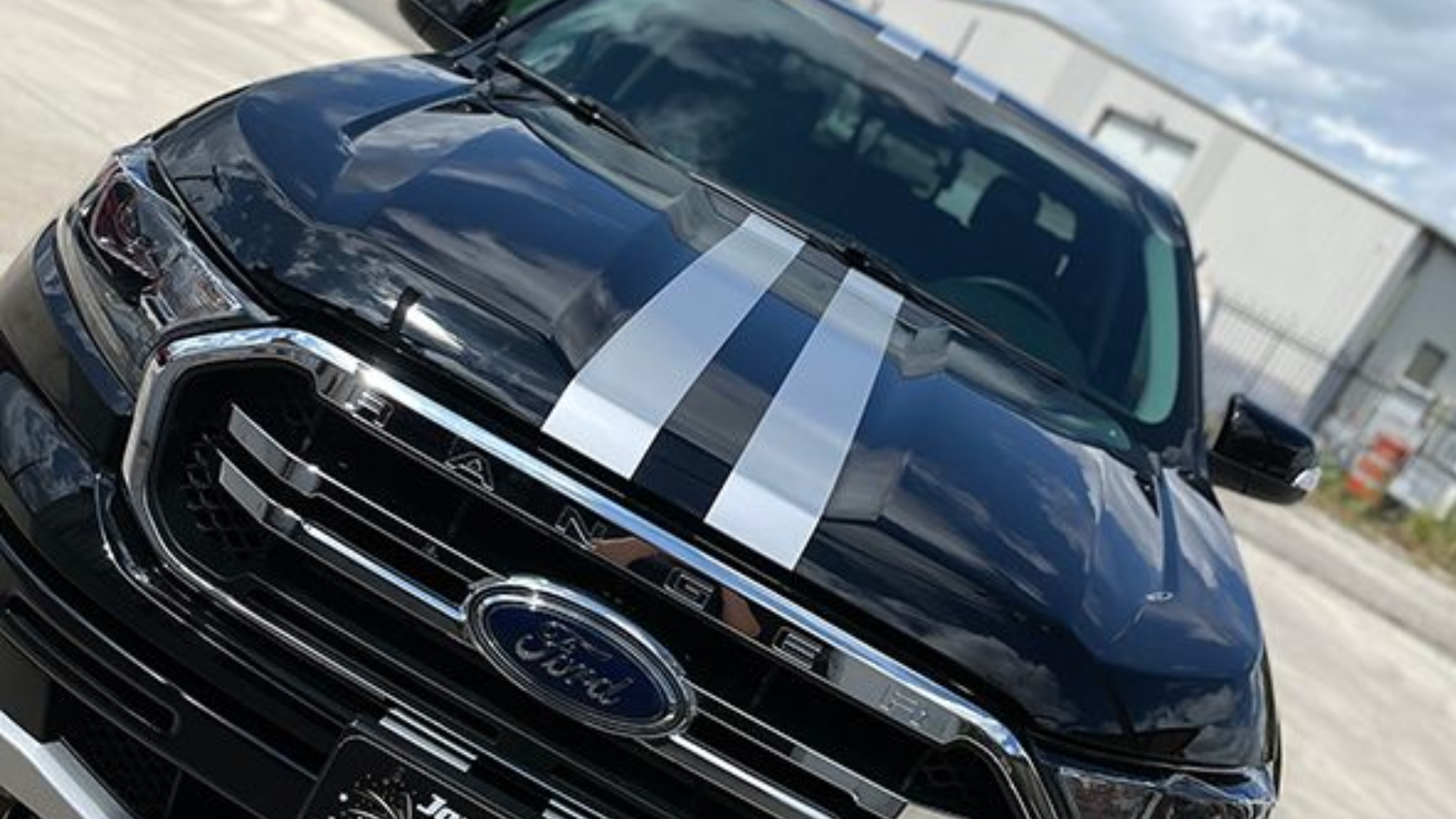 Black Ford SUV with white racing stripes, front view, parked outdoors near a building.