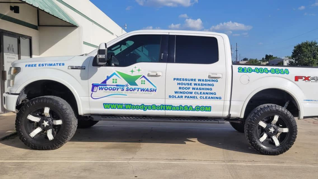 White pickup truck with company logos and contact info parked outside a building in sunny daylight