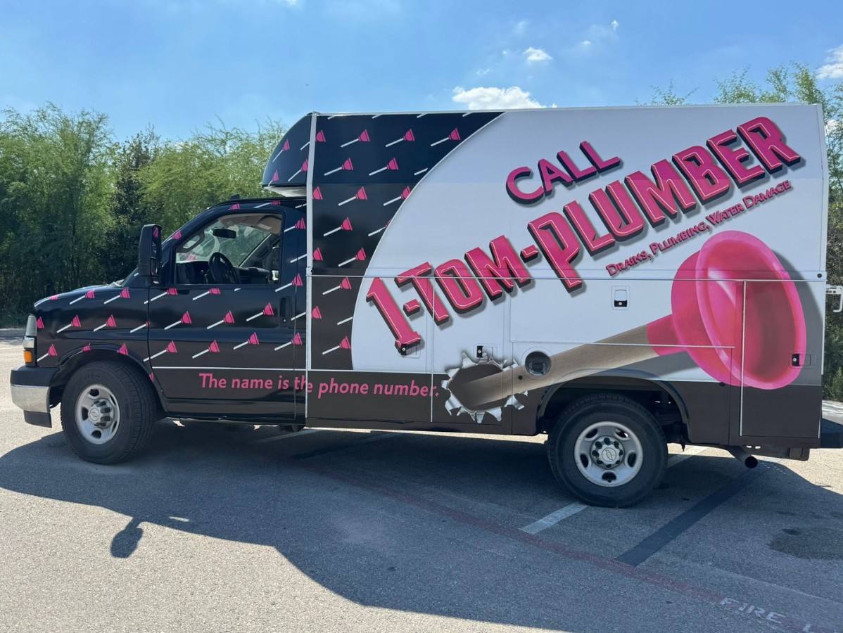 Pink-and-black plumber service truck with large “Call 1-800-Plumber” ad parked outdoors
