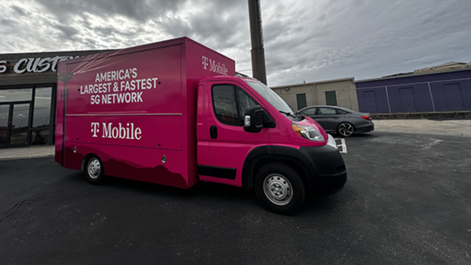 Pink T-Mobile promotional van parked outside a storefront under a cloudy sky