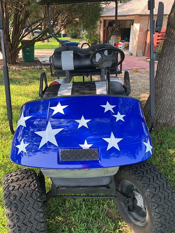 Blue golf cart with white stars parked outdoors on a driveway near a house.